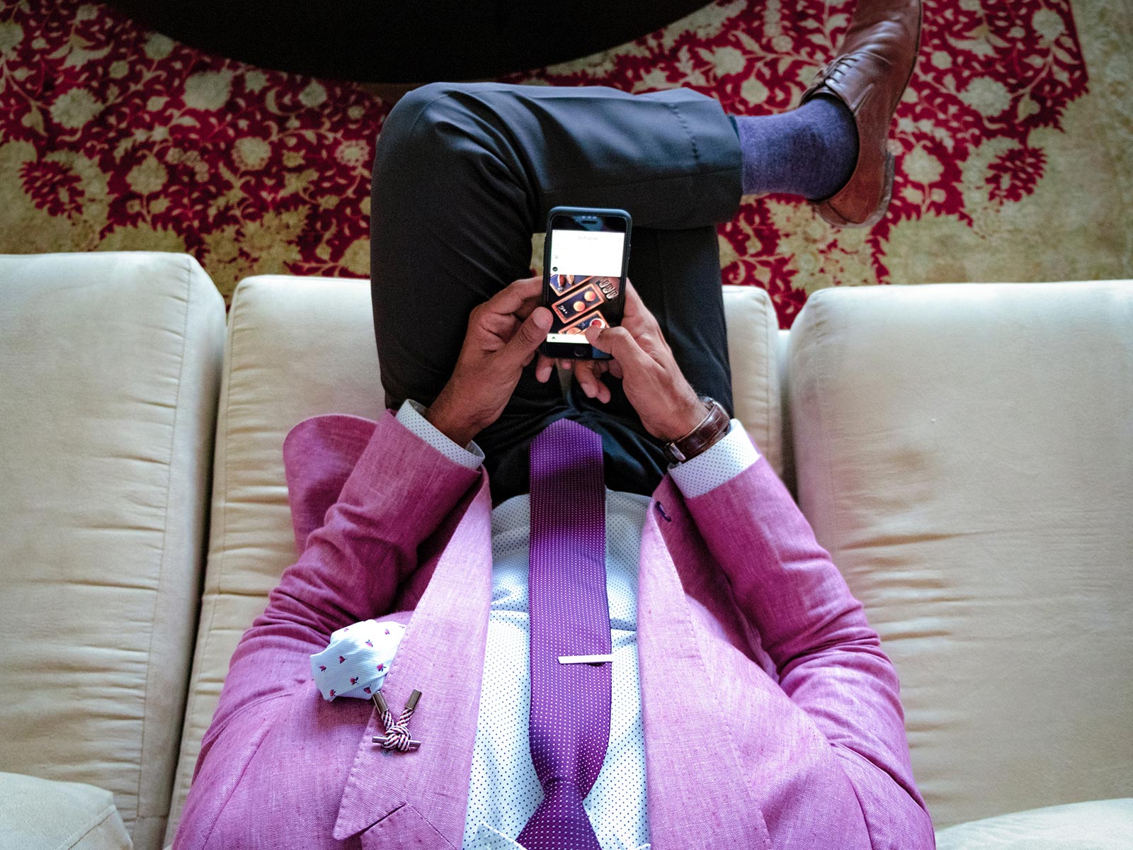 Overhead of man in pink suit on couch looking at phone