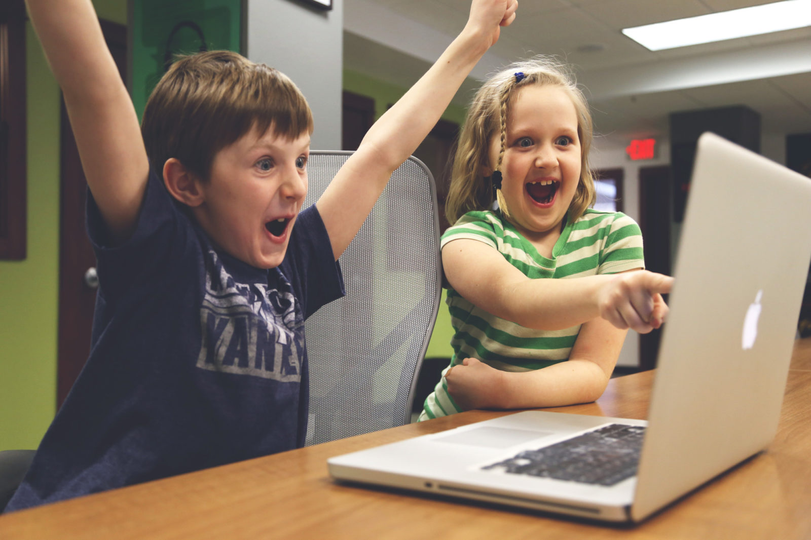 Two children cheering and pointing at a laptop screen.